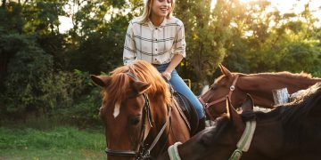 Blonde junge Frau reitet auf ihrem Pferd