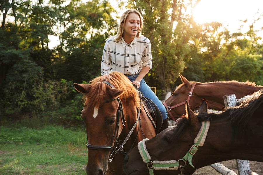 Blonde junge Frau reitet auf ihrem Pferd